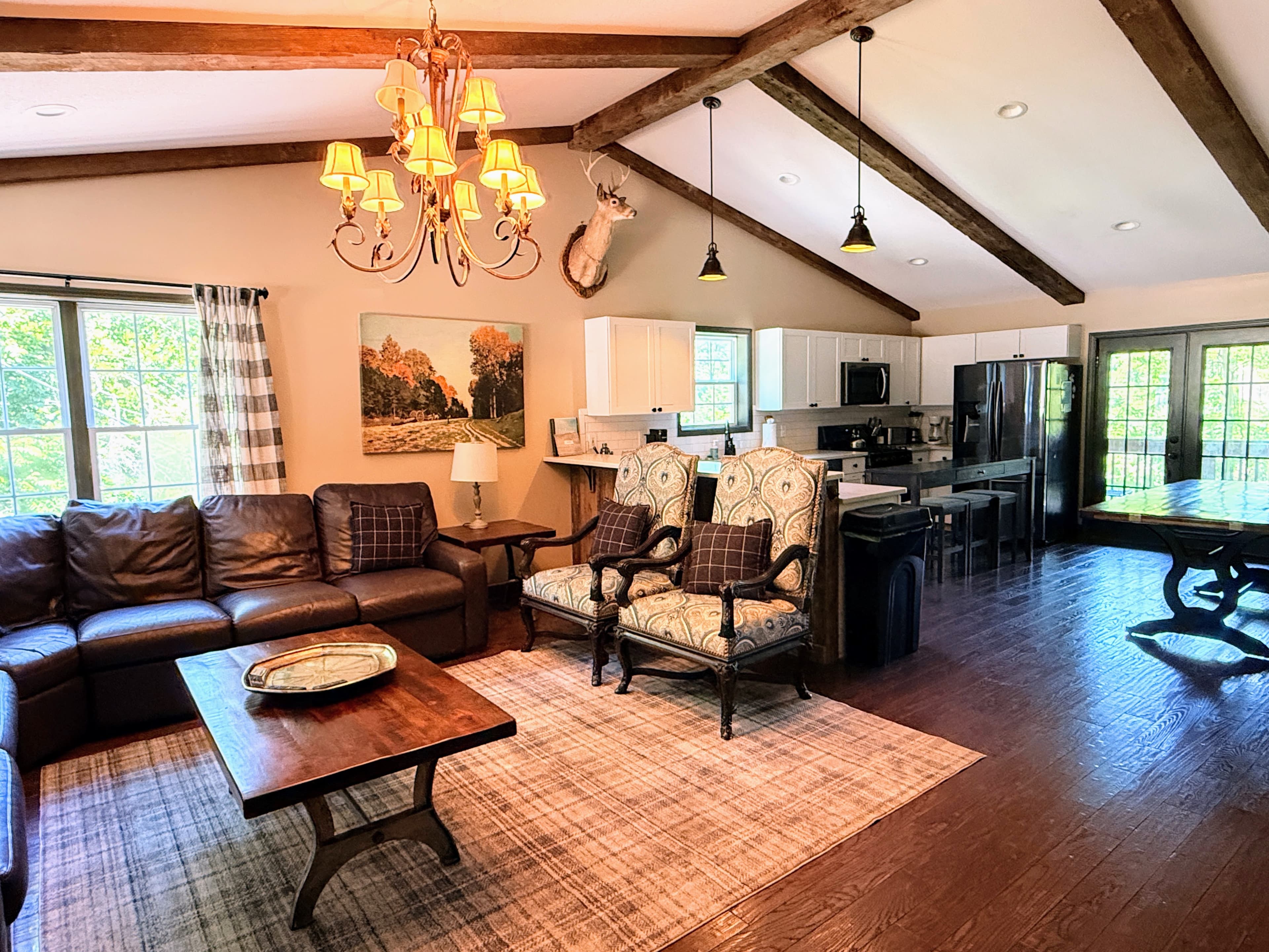 The expansive living room of Livingstone Great House featuring cathedral beamed ceilings, a stone fireplace, and large windows overlooking the North Carolina mountains.