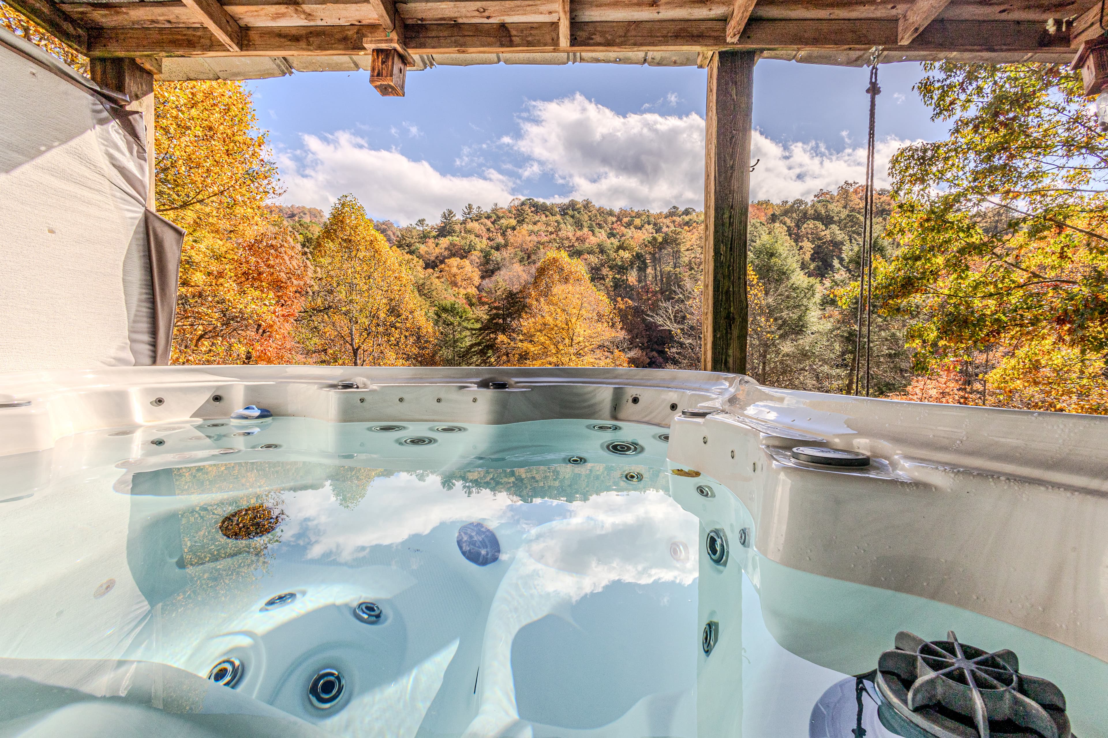 A steaming outdoor hot tub on the covered wooden deck of The Teddy, offering an unobstructed panoramic view of the Smoky Mountain ridgeline in Bryson City