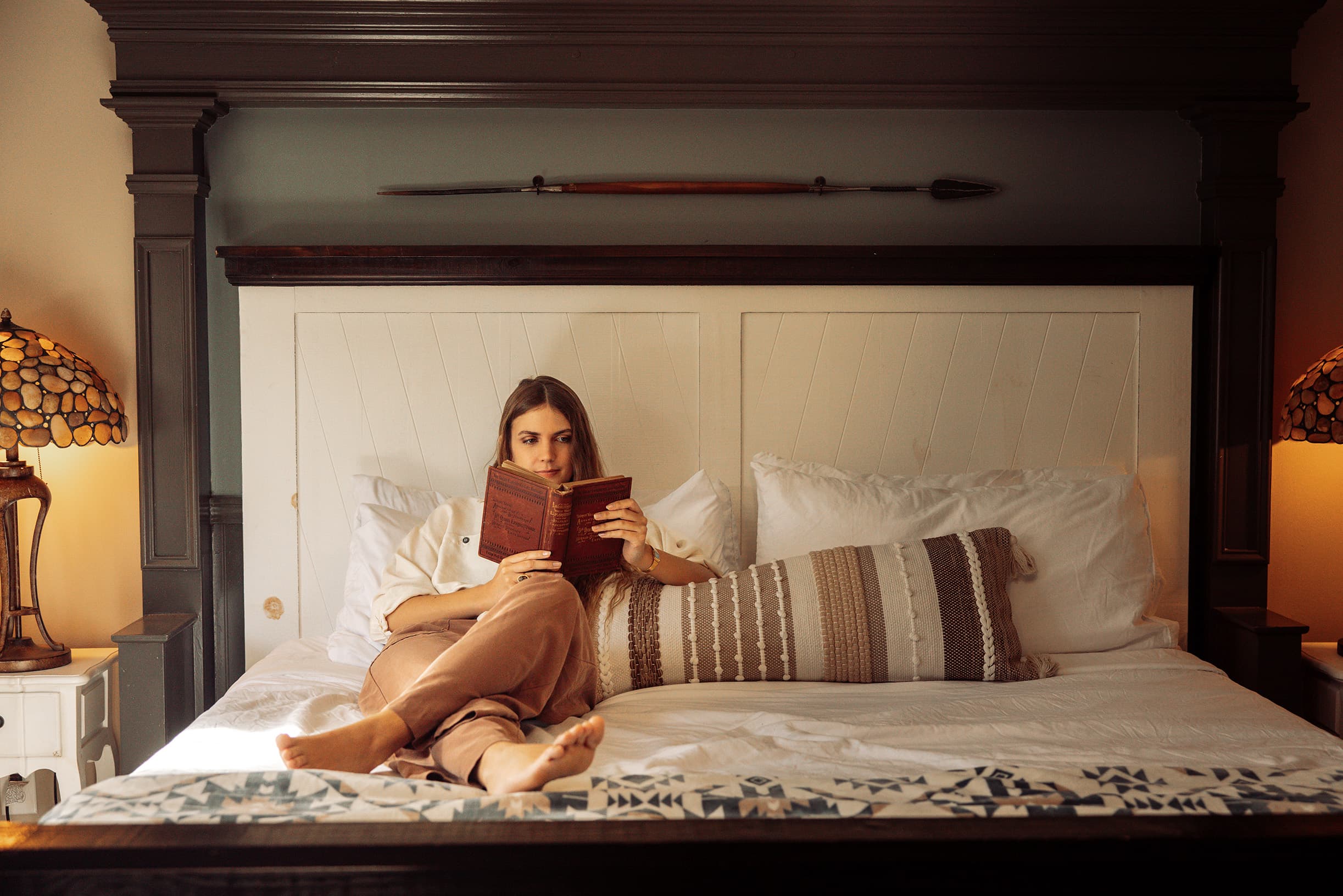 A young woman relaxes on a plush king bed in the David Livingstone Quarters, reading a book while enjoying the mountain ambiance