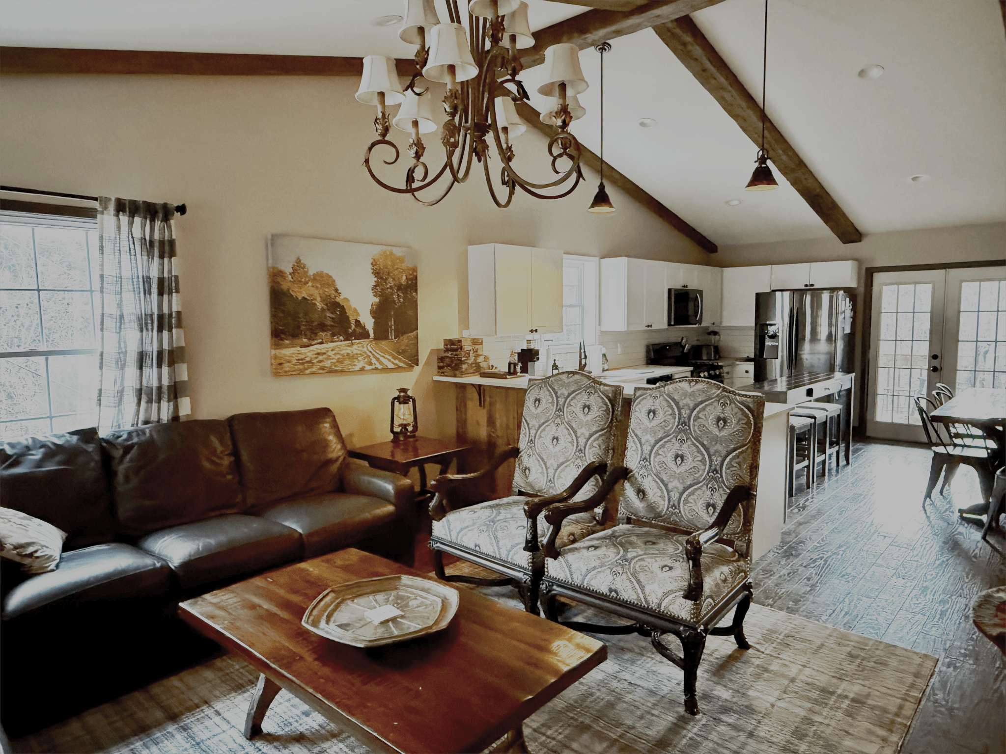 The expansive living room of Livingstone Great House featuring cathedral beamed ceilings, a stone fireplace, and large windows overlooking the North Carolina mountains.