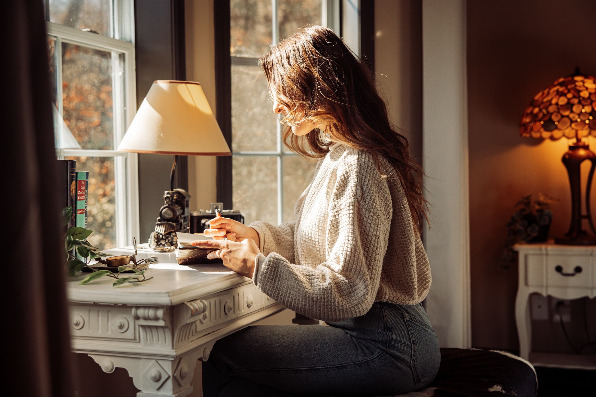A young woman sits at an antique leather-top desk in a bay window at Livingstone Great House, journaling and enjoying the serenity of the mountain ridgeline views.