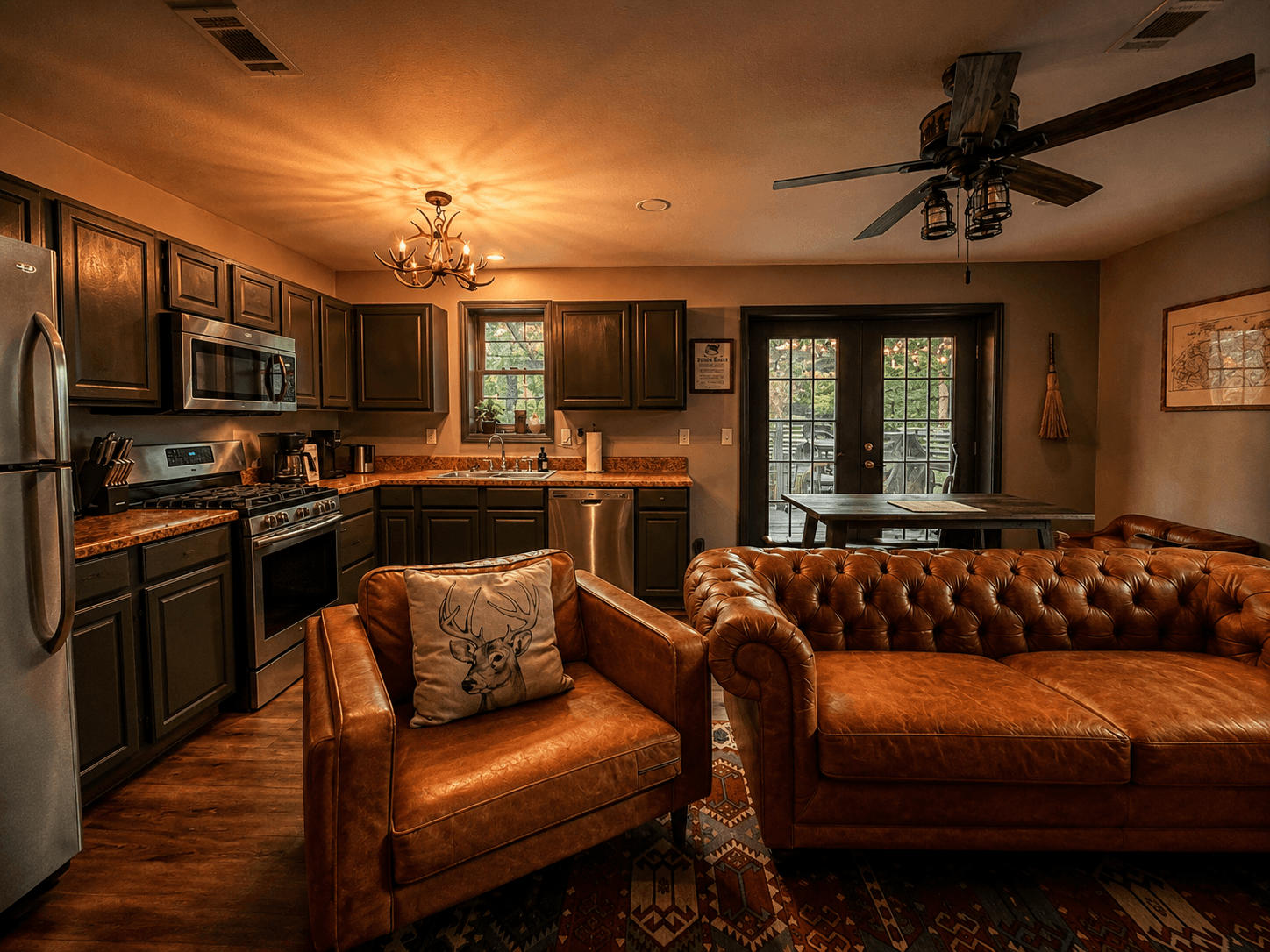 A cozy kitchen and living area featuring dark cabinetry, a leather sofa, and large windows opening to an outdoor space.