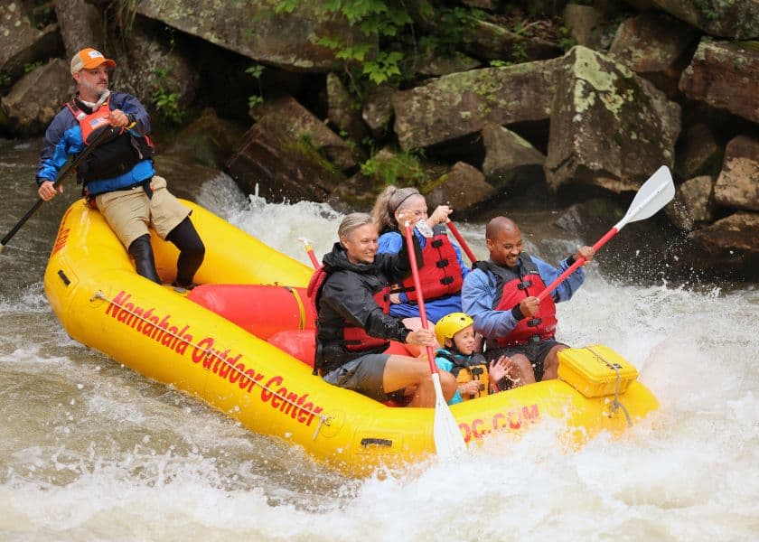A group of five people enjoys white-water rafting in a bright yellow raft on a river surrounded by rocks and greenery. A group of five people enjoys white-water rafting in a bright yellow raft on a river surrounded by rocks and greenery.