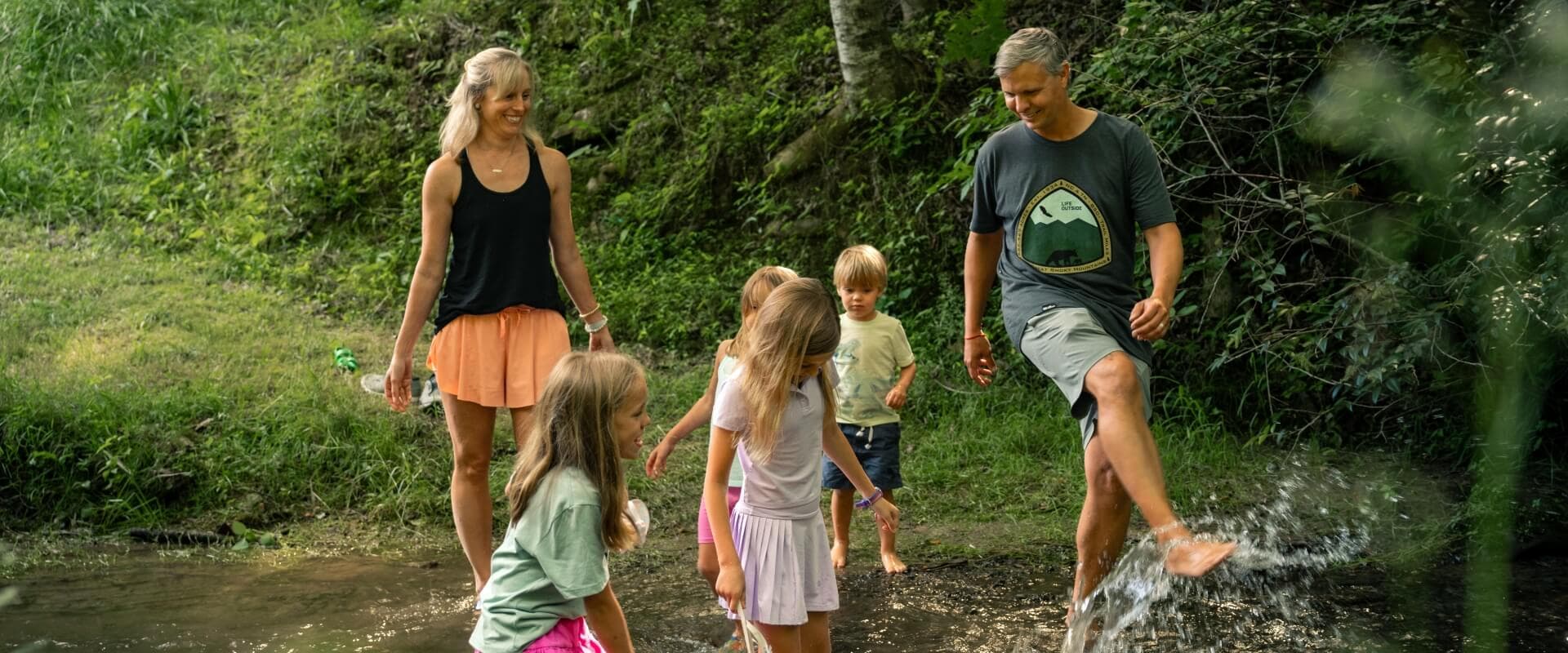 A family plays together in a shallow creek surrounded by greenery.