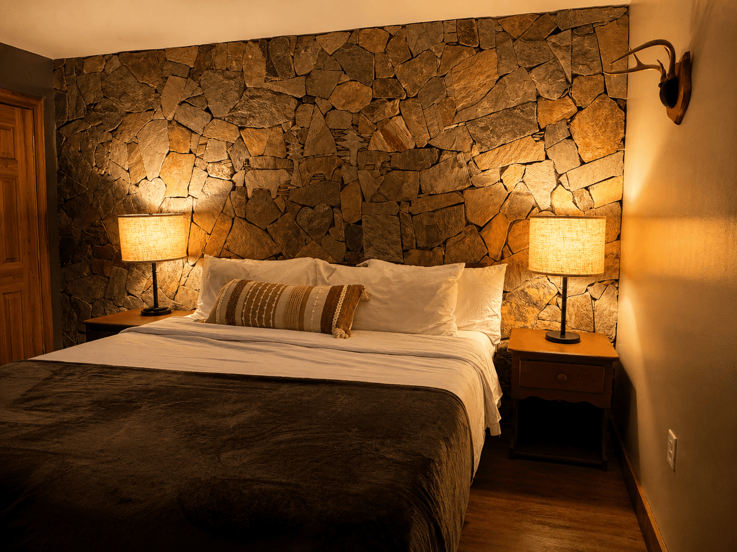 Cozy bedroom featuring a stone accent wall, warm lighting, and a neatly made bed.
