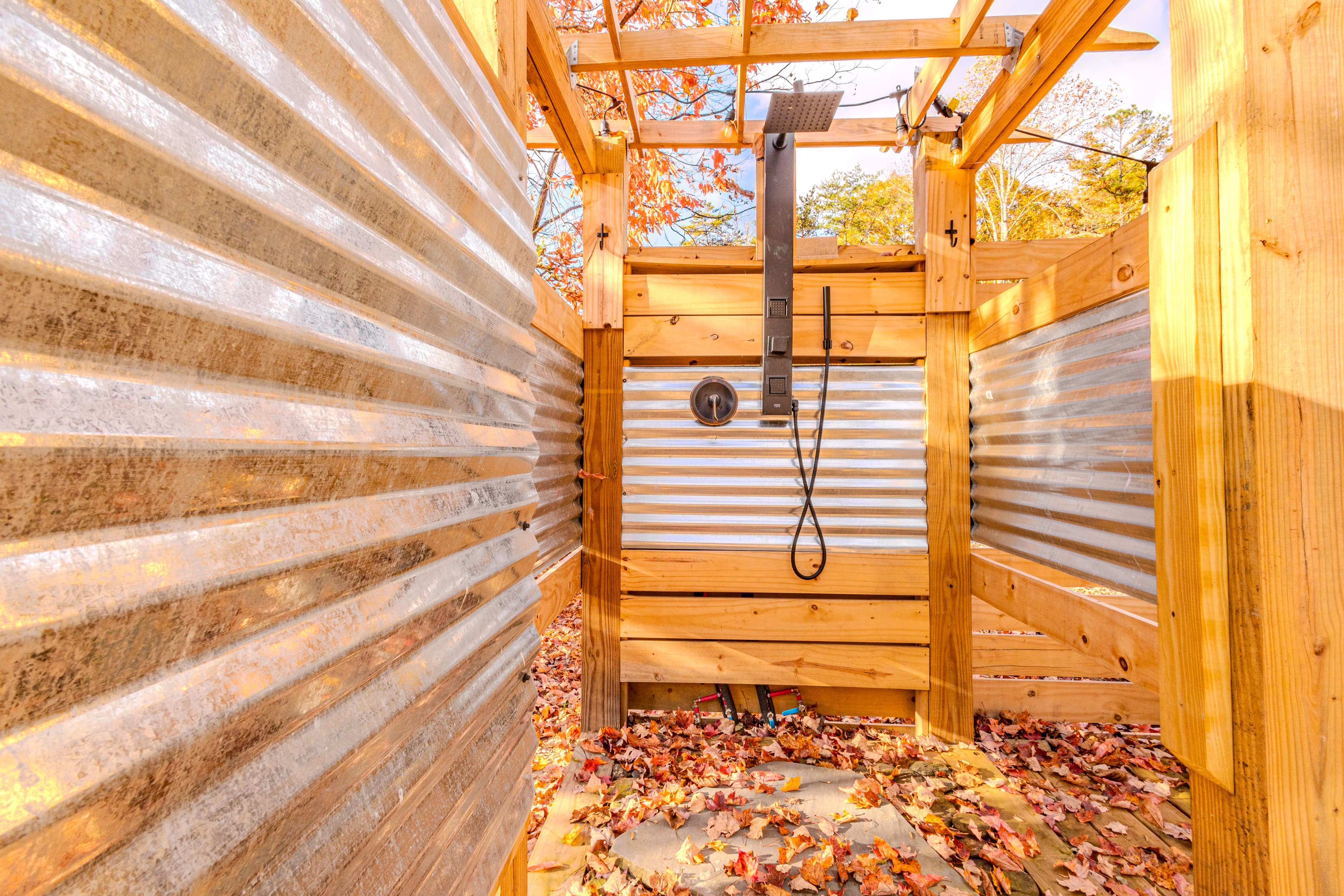 Outdoor shower enclosed by wooden and metal walls with fallen leaves on the ground.