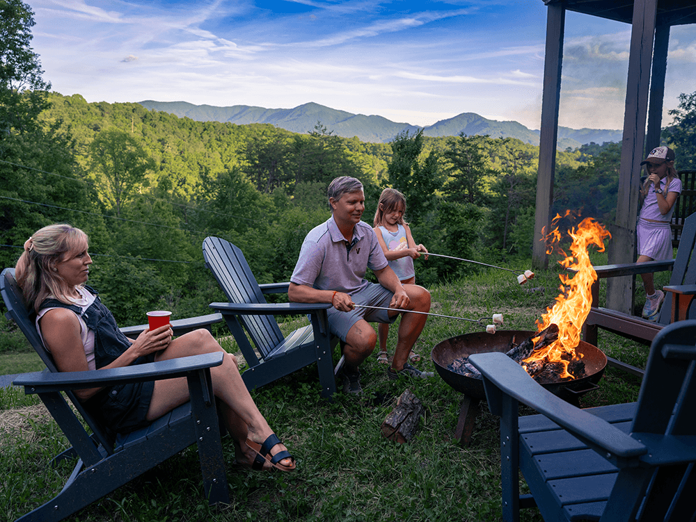 A family enjoys a campfire in a scenic outdoor setting, roasting marshmallows and relaxing in Adirondack chairs.