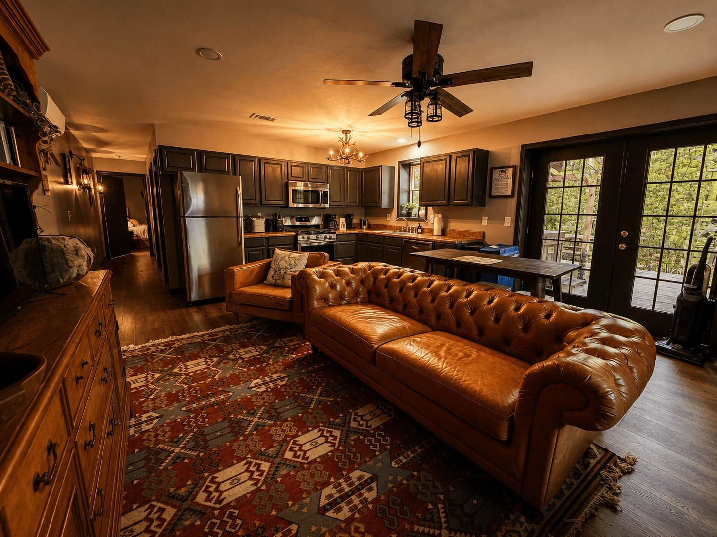 A cozy, rustic living space featuring a brown leather sofa, wooden cabinets, and a vibrant area rug.