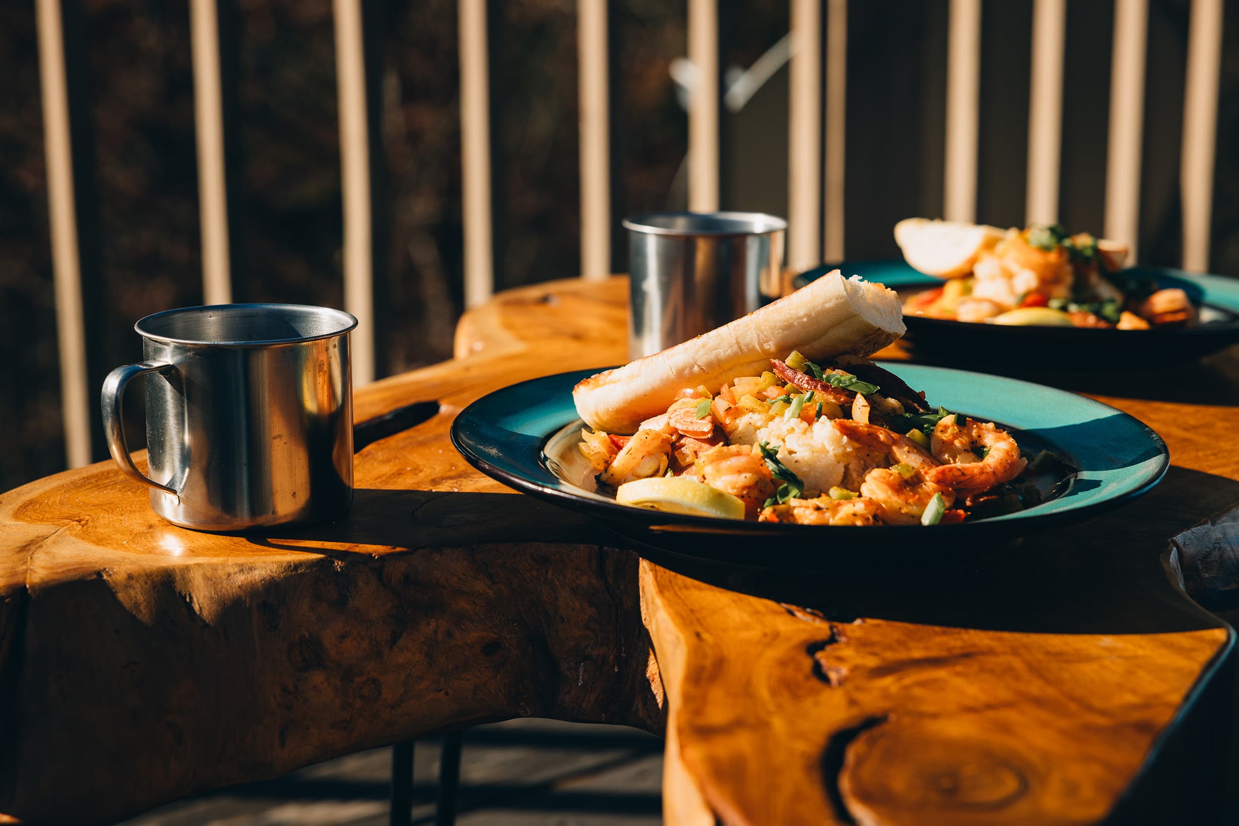 A plate of shrimp and vegetables with a tortilla and a metal cup on a wooden table.