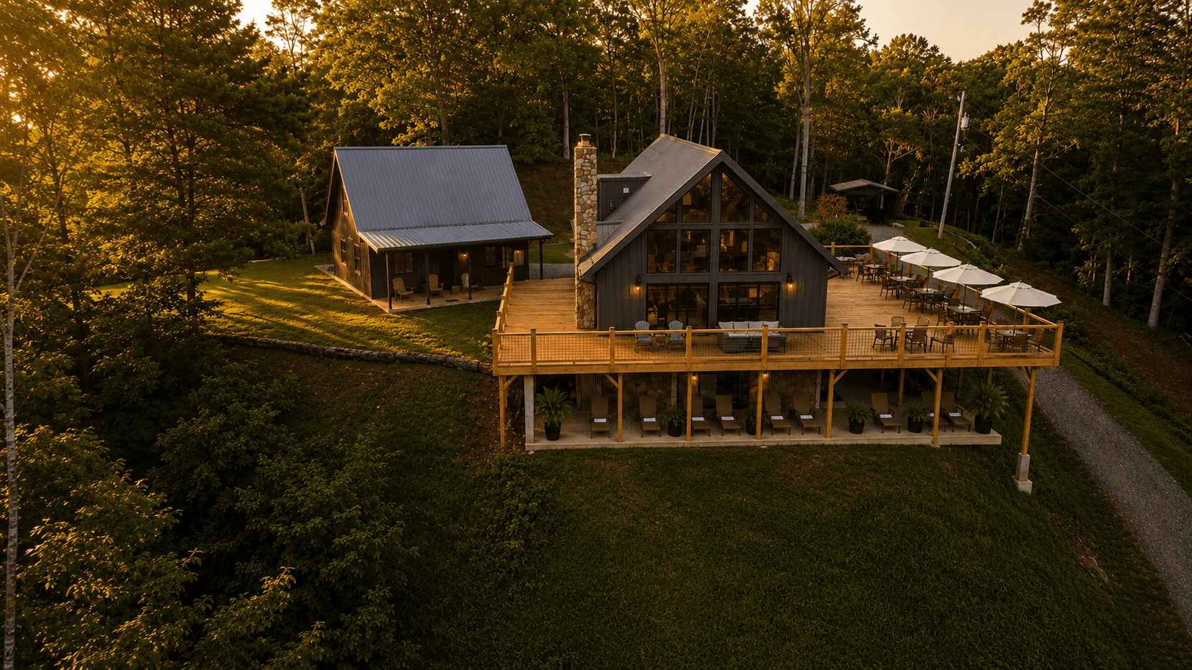 A modern cabin with a spacious deck overlooks a forested area at sunset.