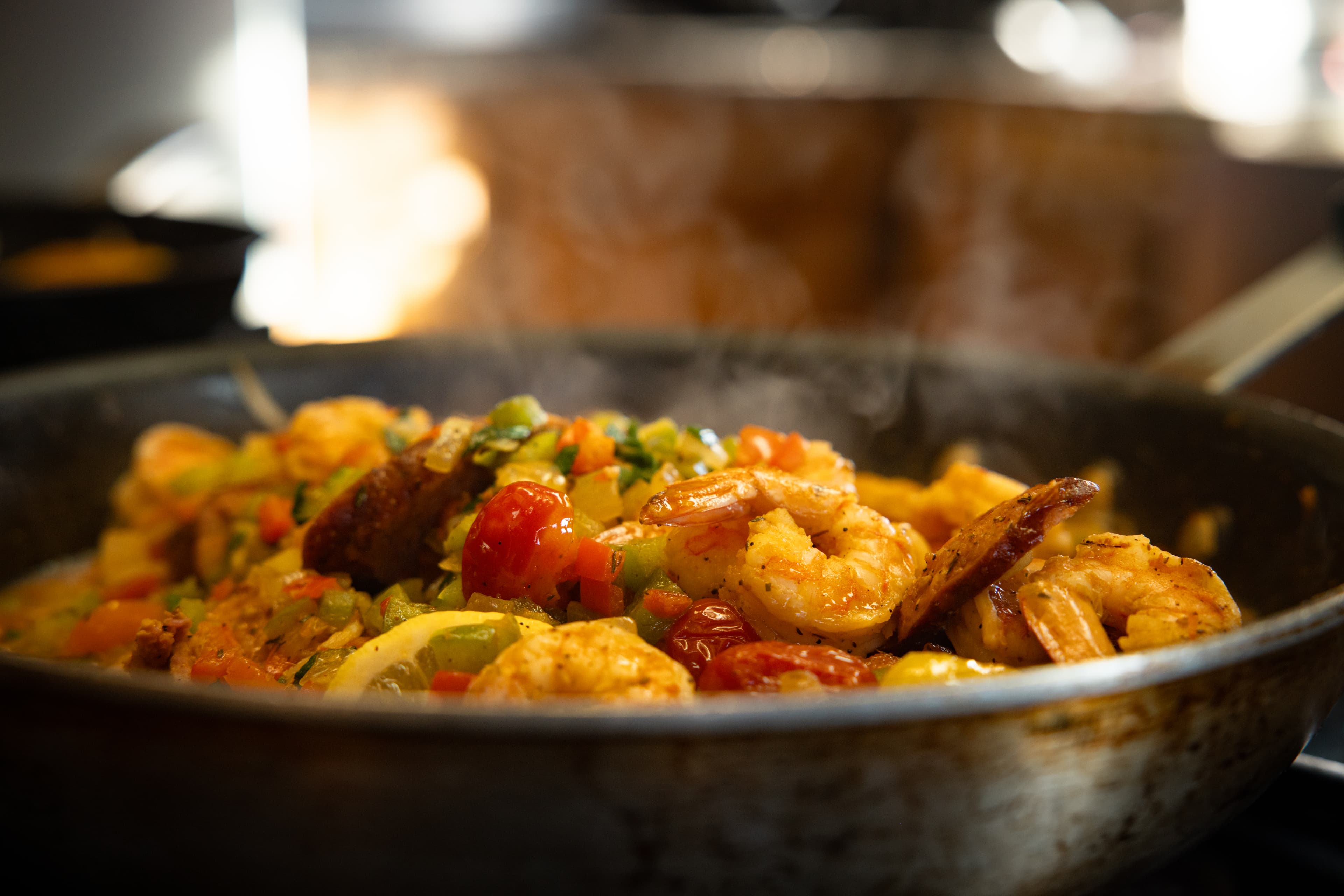 A sizzling skillet filled with shrimp, vegetables, and spices emitting steam.