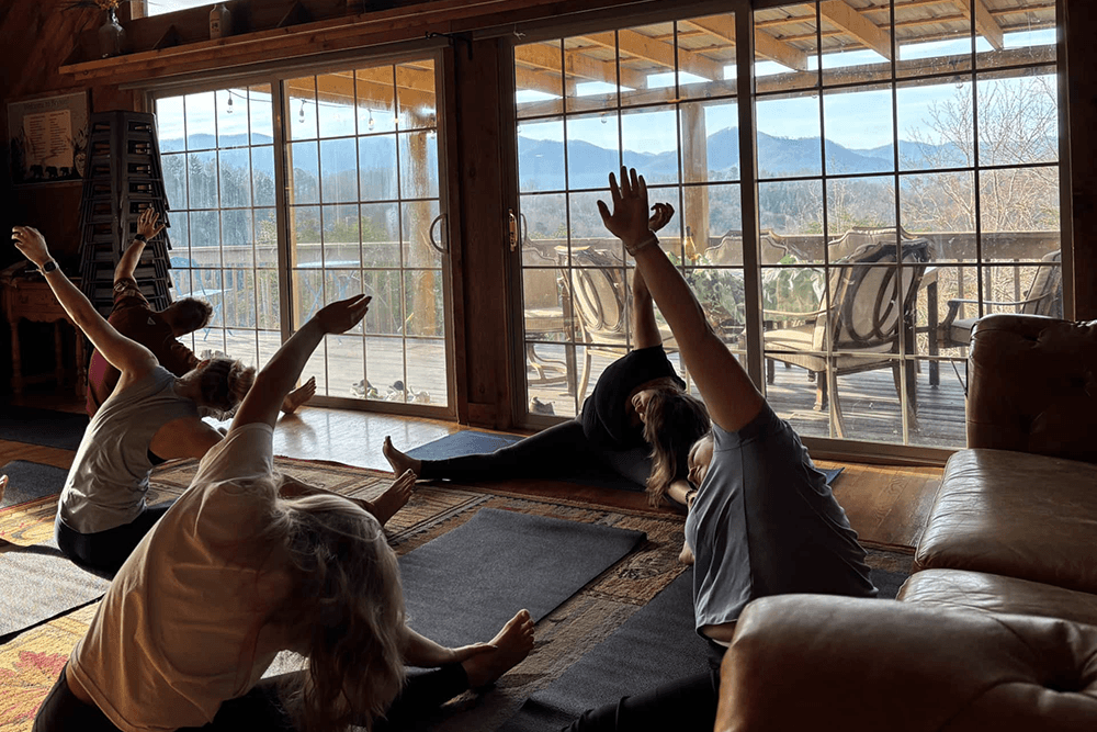 A group of people practicing yoga indoors with large windows showing a mountain view.