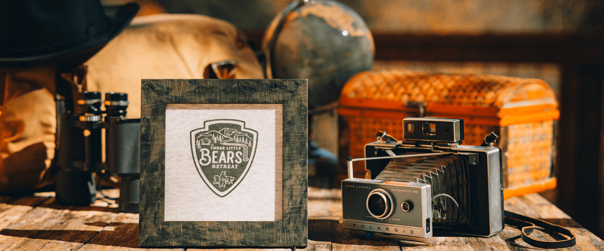 A framed logo reading "Texas Little Bears Retreat" surrounded by vintage cameras, binoculars, and travel items.