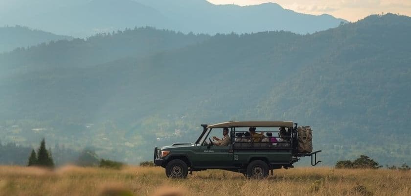 safari-style vehicle in an open field with mountains in the background